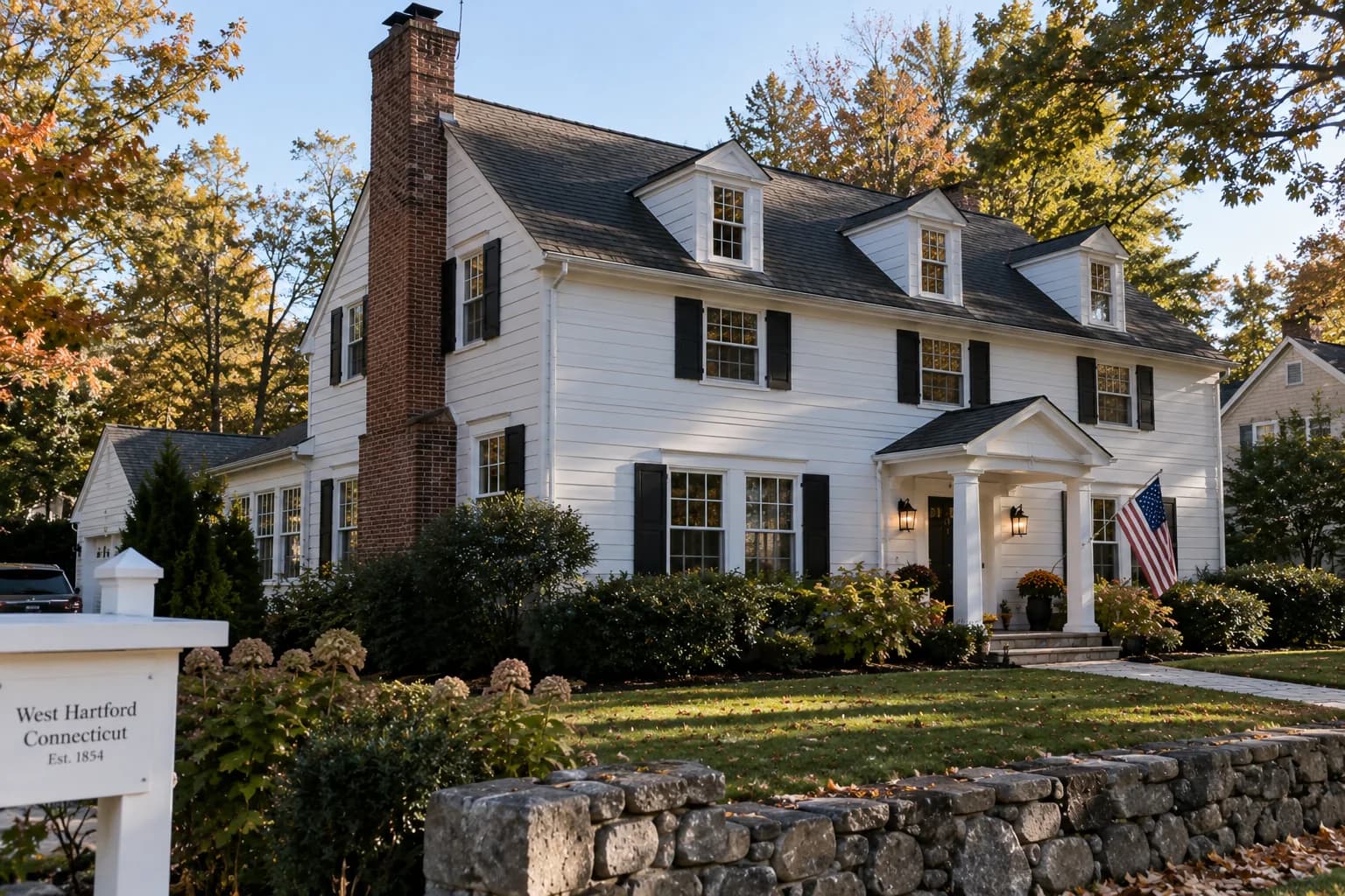 New England street of clapboard and colonial houses with brick chimneys against an autumn sky.